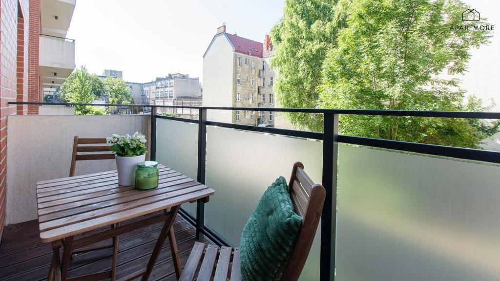 Small balcony with wooden table and chairs, green cushion and leafy street view.