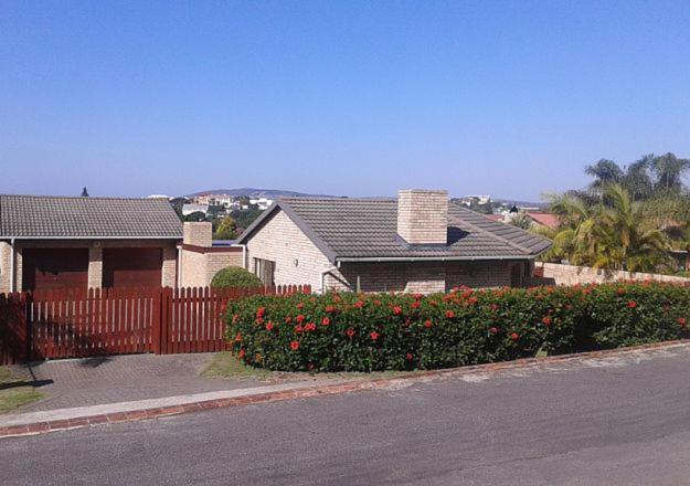 a house with a fence and a yard with flowers at Pladda in Plett in Plettenberg Bay