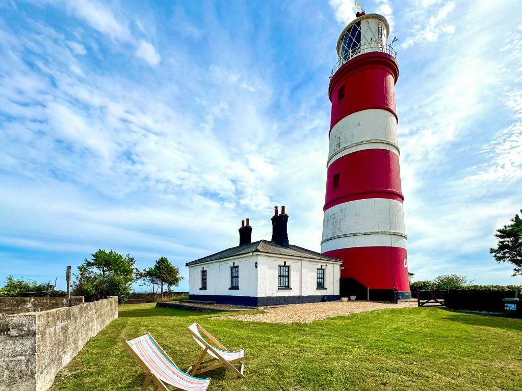 a red and white lighthouse with a house and two chairs at Lighthouse Cottage in Happisburgh
