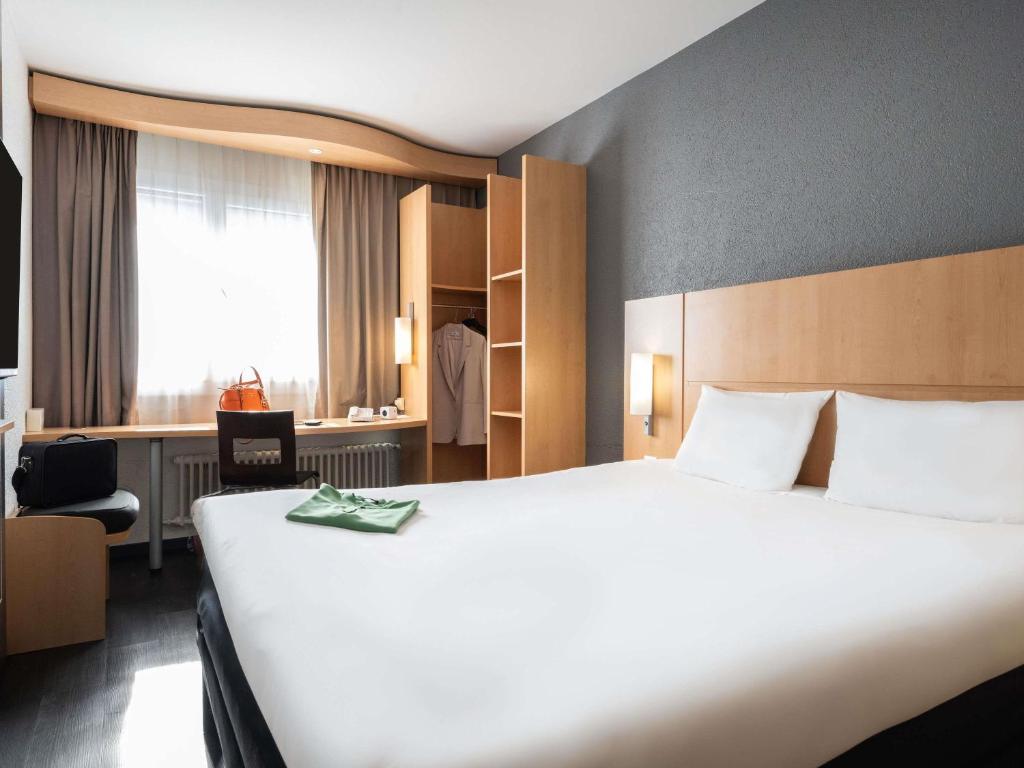 Una habitación de hotel con una gran cama blanca y una silla. en ibis Genève Centre Gare, en Ginebra
