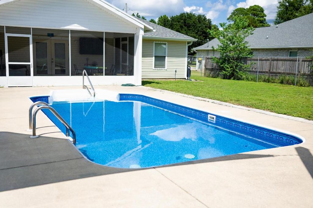 a blue swimming pool in a yard next to a house at The Breeze in Navarre