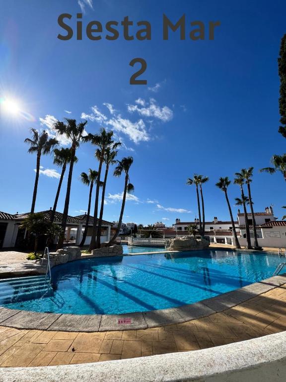 a swimming pool with palm trees and a blue sky at El Minorq'In in Cala en Porter