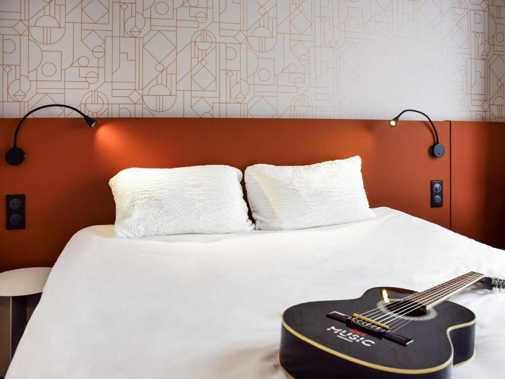 a guitar is sitting on a bed with a white bed at ibis Rodez Centre in Rodez