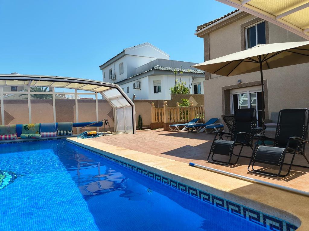 een zwembad met stoelen en een parasol naast een huis bij Villa with super swimming pool in Gran Alacant