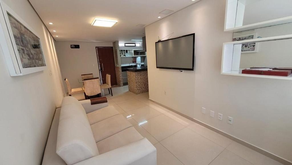 a living room with a couch and a tv on a wall at Cantinho do Caribe Paraibano in João Pessoa