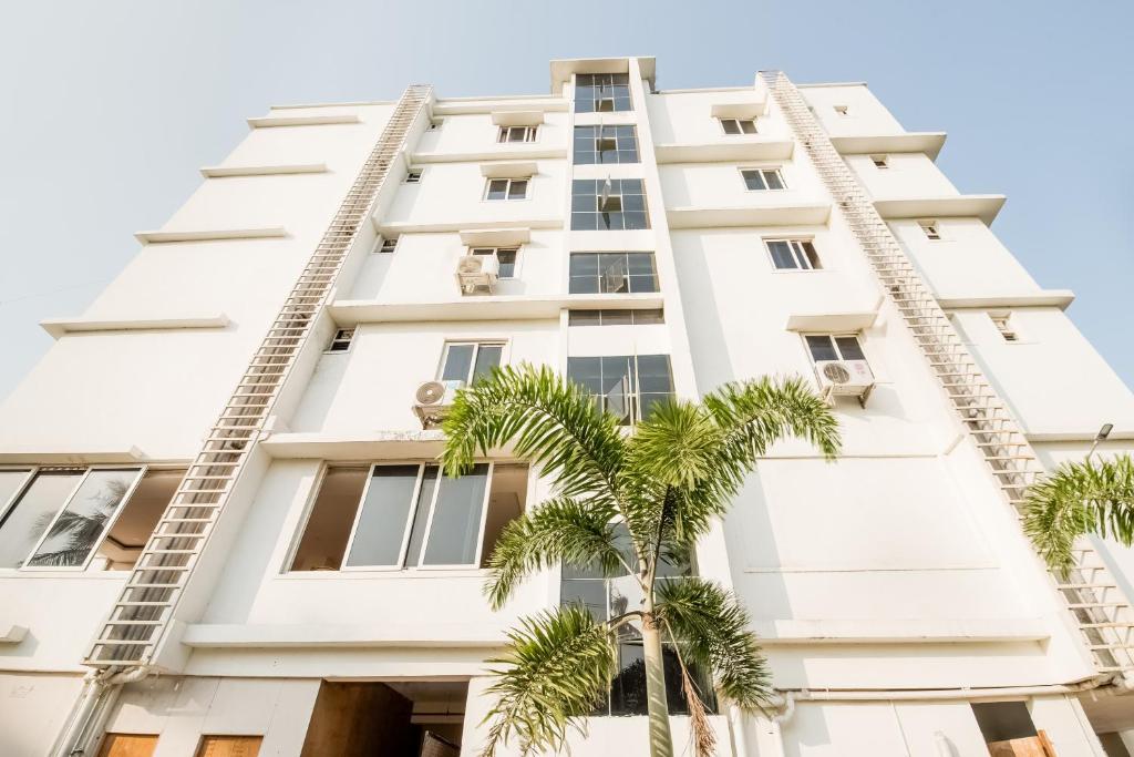 a tall white building with palm trees in front of it at Hotel O Ram Nivas in Kurmannapalem
