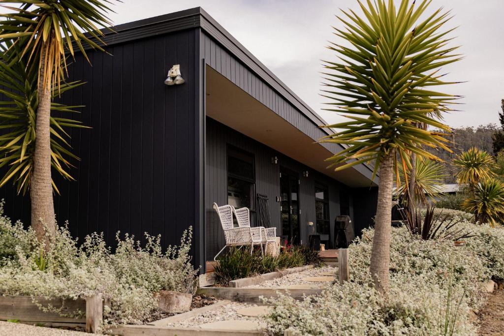een zwart huis met twee witte stoelen en palmbomen bij Lifebuoy Beach House Bicheno in Bicheno