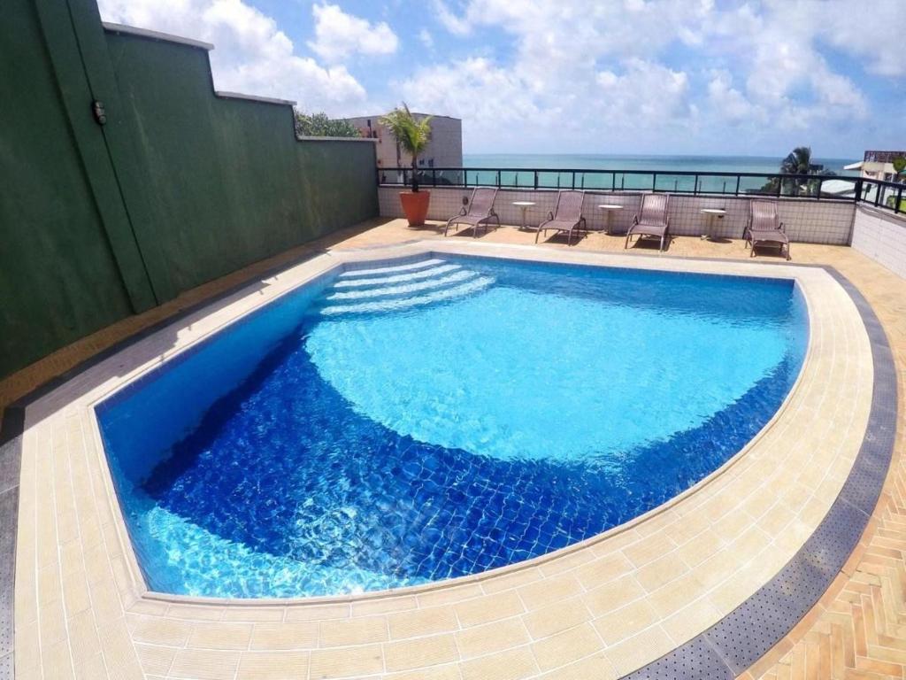 une piscine avec des chaises et l'océan en arrière-plan dans l'établissement Quality suites natal apto 1009, à Natal