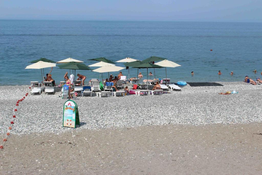 a group of people sitting on a beach with umbrellas at Fish House Guest House in Gagra