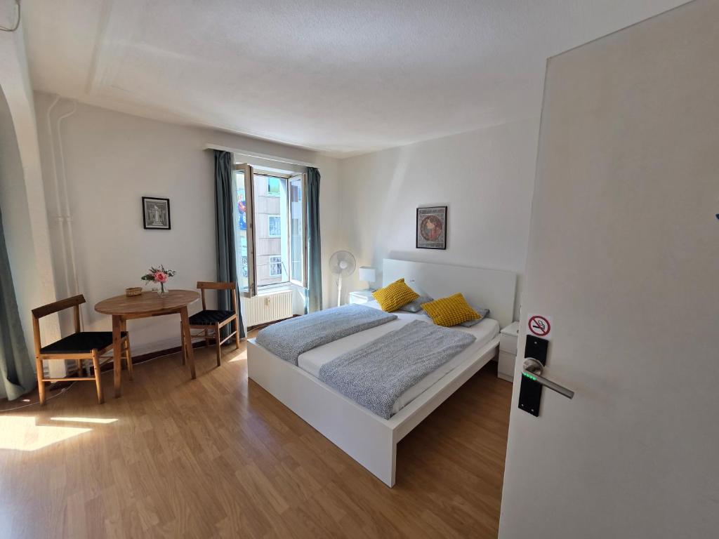 a white bedroom with a bed and a table at Julia Zimmer Luzern in Luzern