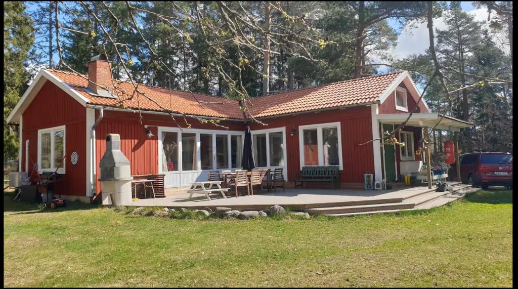 una pequeña casa roja con porche y sillas en Spersboda 2 barnvänliga hus sjöutsikt & VARM pool Spersboda, en Spersboda