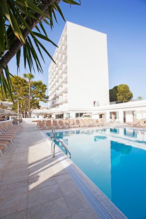 a hotel swimming pool with chairs and a building at Grupotel Farrutx in Can Picafort