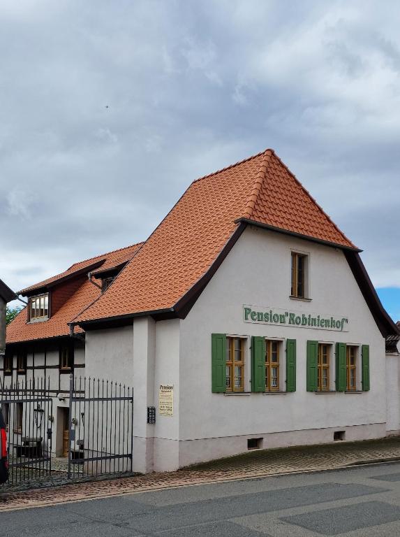 a building with a red roof and green windows at Pension Robinienhof in Schadeleben
