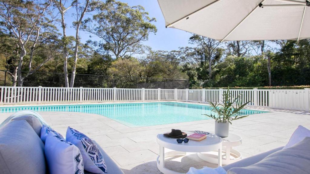 - une piscine avec une clôture blanche, une table et un parasol dans l'établissement Resort Style Living With Pool, Tennis Court and Beach, à Avoca Beach