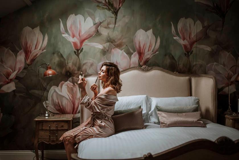 a woman sitting on a bed with flowers on the wall at Woodhill Country House in Otterburn