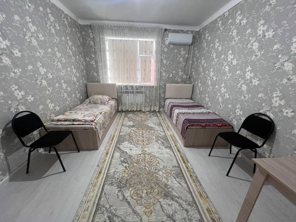 a bedroom with two beds and two chairs and a window at Aral Guest House in Aralʼsk