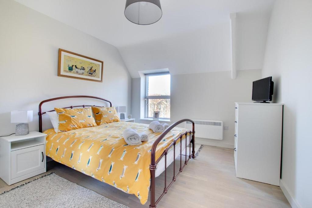 a bedroom with a bed with yellow sheets and a refrigerator at Daisy’s - Ellinbrook Apartments in Hunstanton