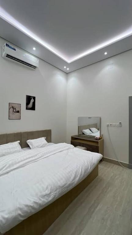 a white bedroom with a bed and a night stand at moon night in Al Kharj