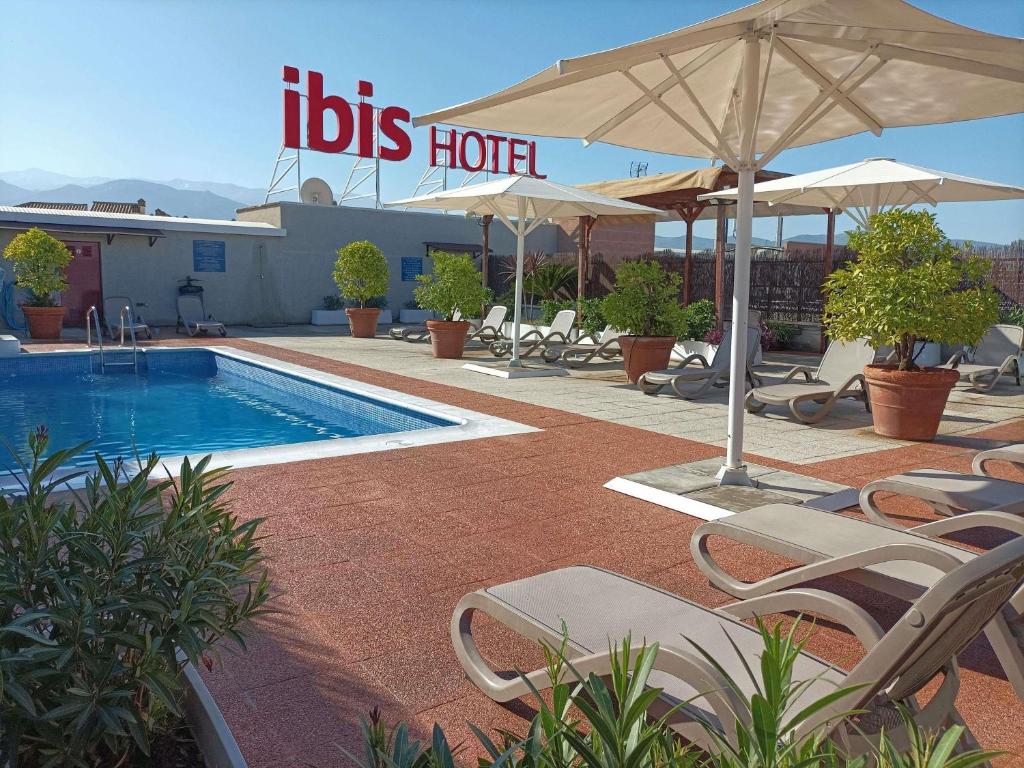 a pool with chairs and umbrellas next to a hotel at Ibis Granada in Granada