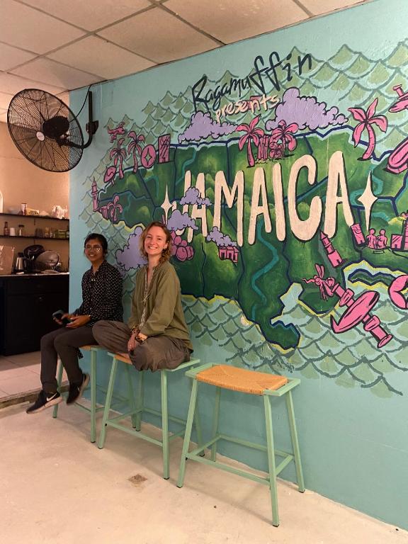 two people sitting on a bench in front of a mural at Ragamuffin Hostel in Kingston