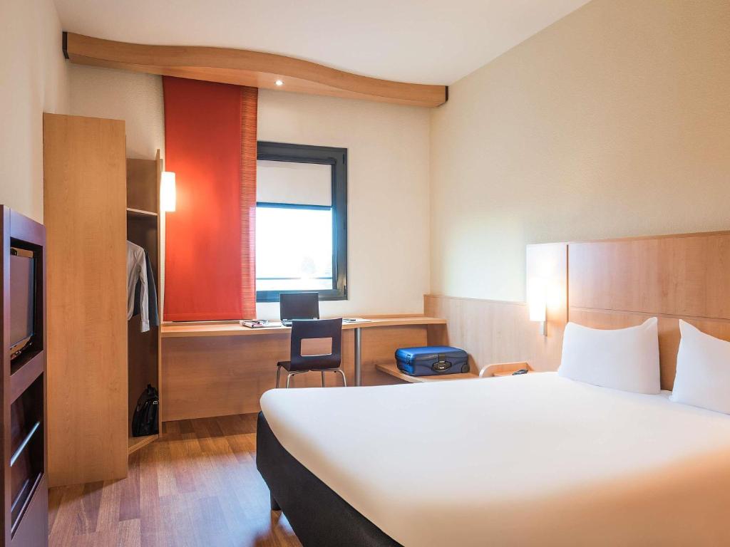 a hotel room with a bed and a desk and a window at Hotel Ibis Milano Malpensa in Cardano al Campo