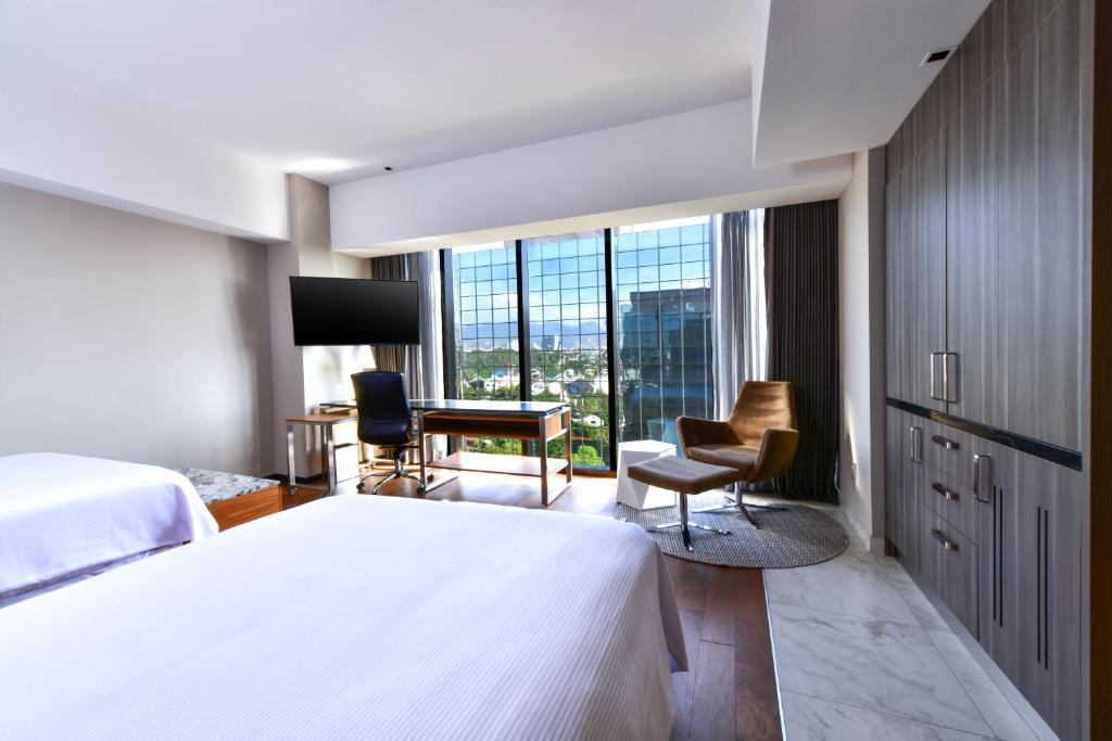 A bright bedroom with a large bed, window-side desk and lounge chair.