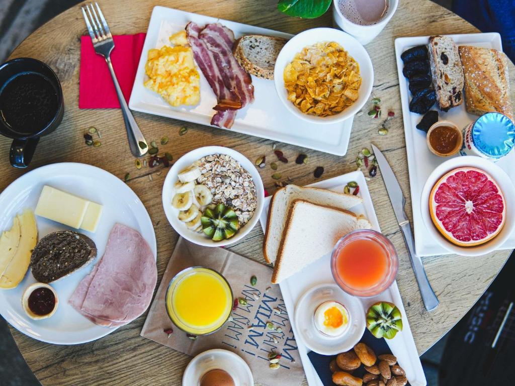 ein Holztisch mit Tellern mit Frühstücksspeisen und Getränken in der Unterkunft ibis Caen Porte De Bretagne in Bretteville-sur-Odon