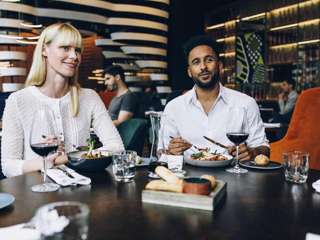 a man and woman sitting at a table eating food at PULLMAN Berlin Schweizerhof - City Center, Zoo und Kurfürstendamm in Berlin