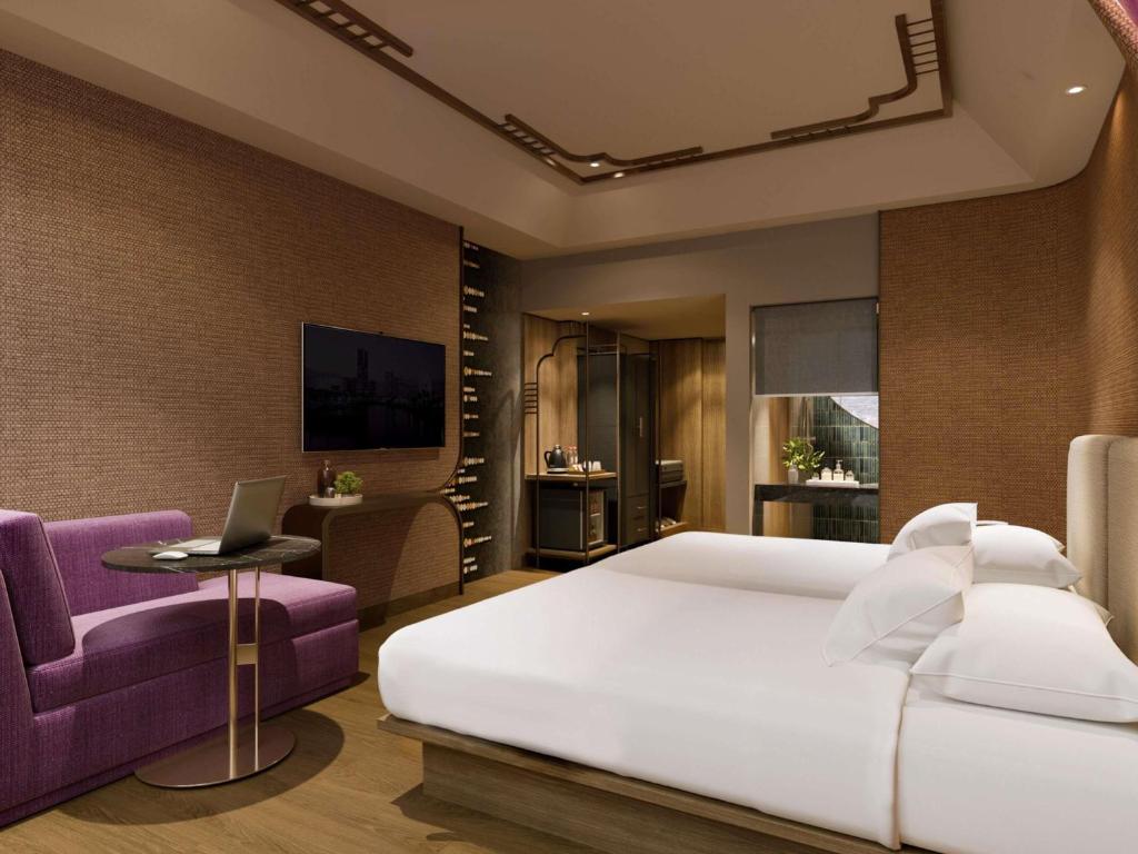 a bedroom with a large white bed and a purple chair at Mercure Surabaya Grand Mirama in Surabaya