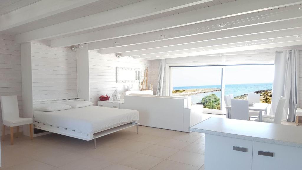 a white bedroom with a bed and a view of the ocean at Casa Dansodà sul mare in Torre Lapillo