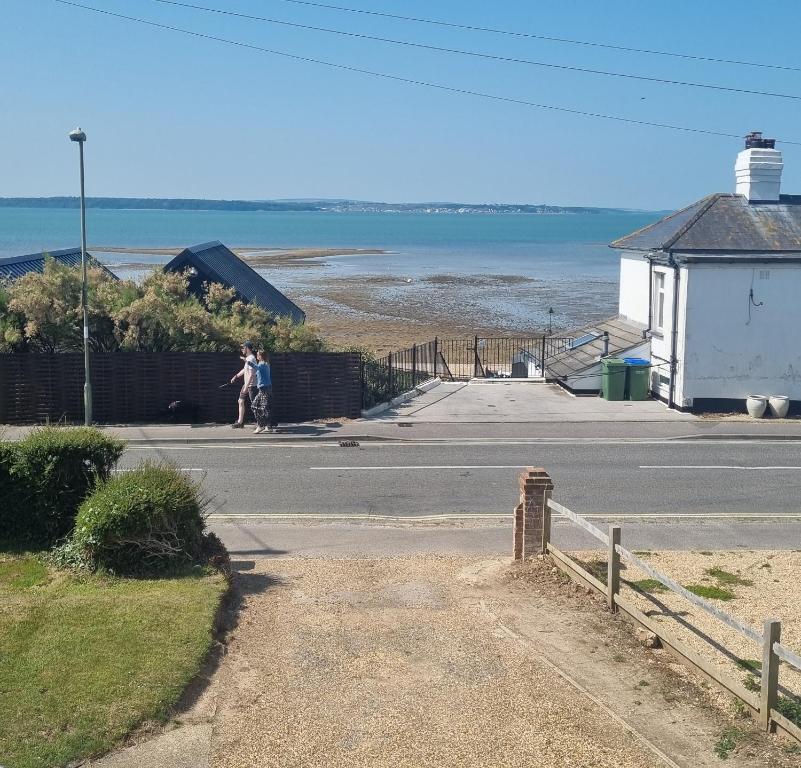 Dos personas caminando por una calle cerca de un faro. en Hill Head - Large cottage with sea views - 5 bed, slp 10, en Hill Head