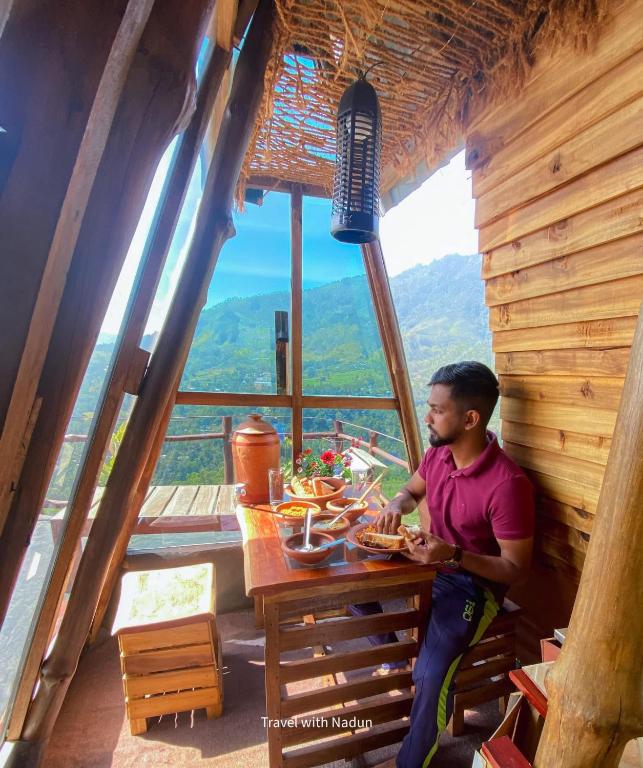 a man sitting at a table in a cabin at prince's place cabins and camping in Badulla