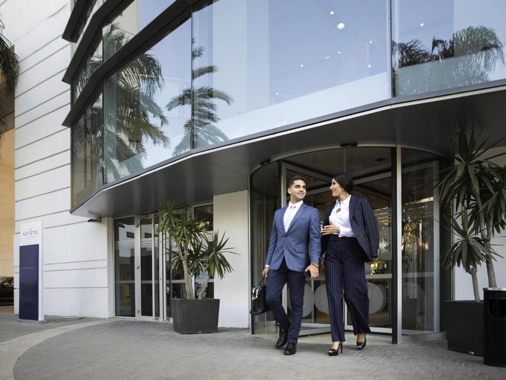 Due uomini in giacca e cravatta che camminano fuori da un edificio. di Novotel Casablanca City Center a Casablanca