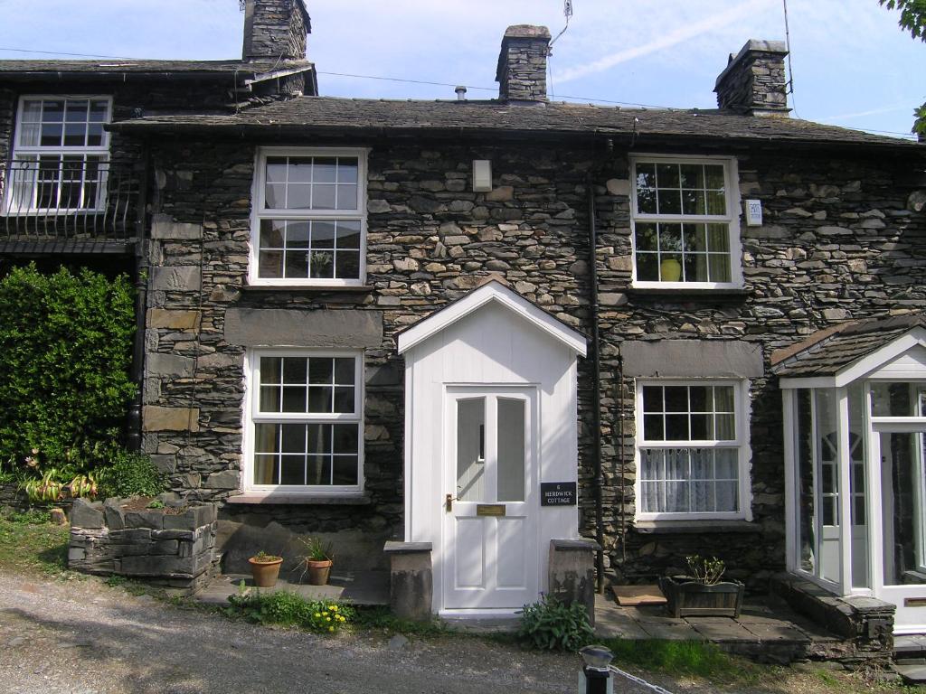an old stone house with a white door at Herdwick Cottage in Troutbeck Bridge