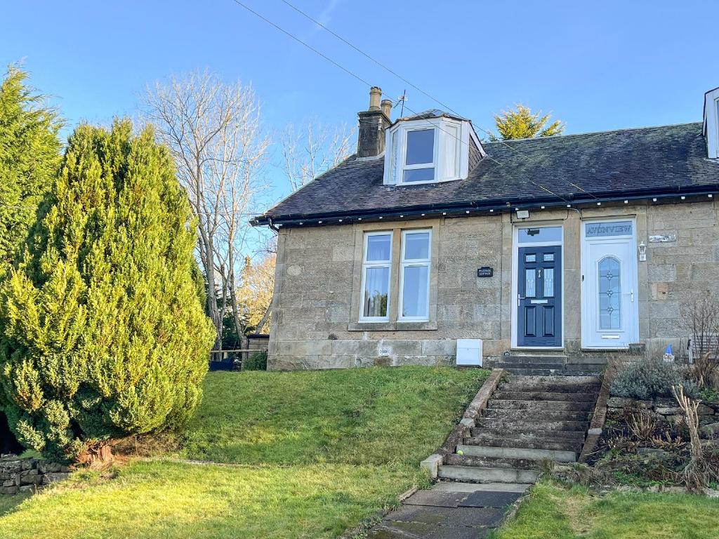 a brick house with a blue door and a tree at Riverside Cottage in Larkhall
