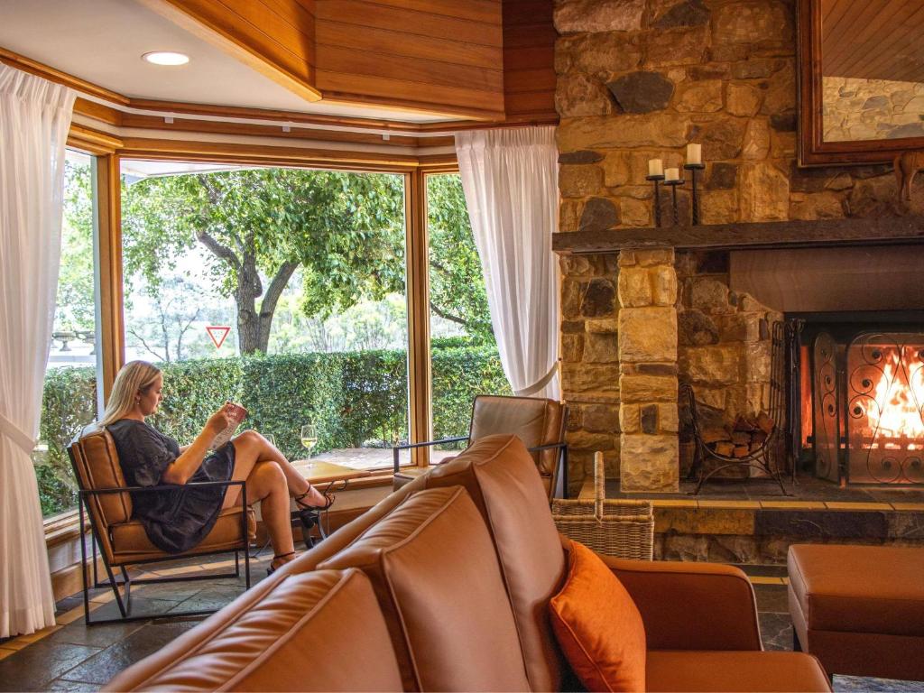 a woman sitting in a chair in a living room with a fireplace at Mercure Hunter Valley Gardens in Pokolbin