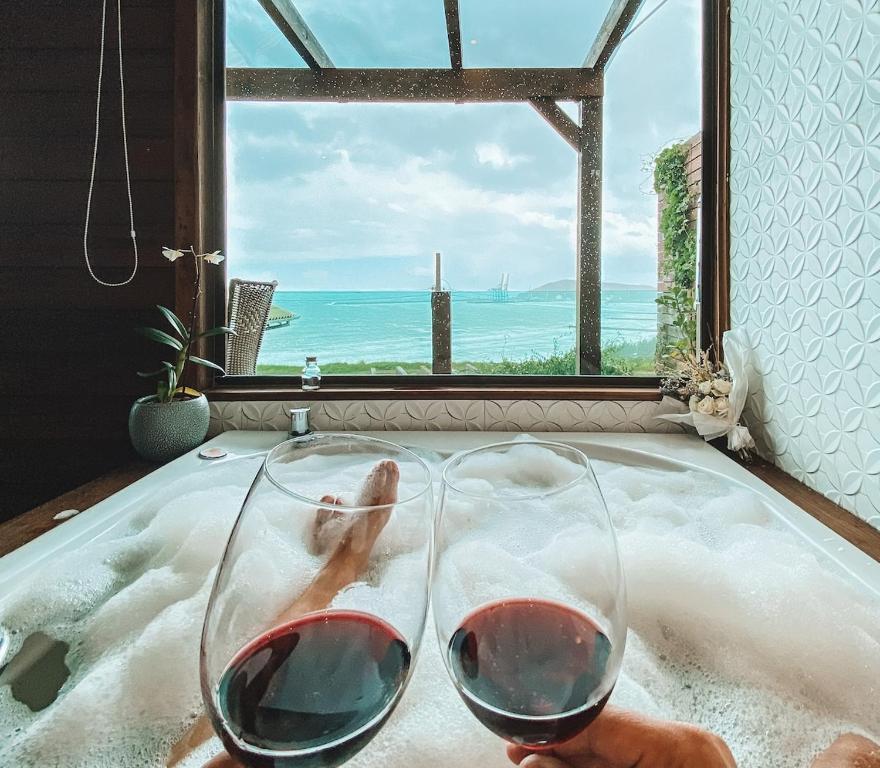 two glasses of wine in a bath tub with a window at Chalés Mirante da Zimba in Imbituba