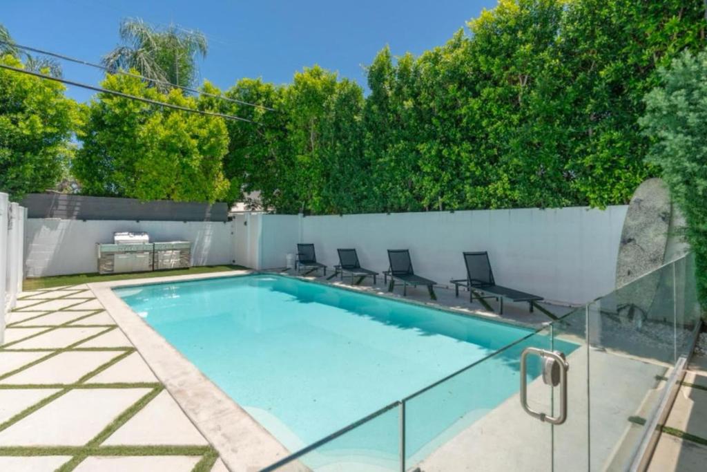 a swimming pool with chairs next to a fence at Modern Encino Retreat with pool, lush yard and comfort in Encino
