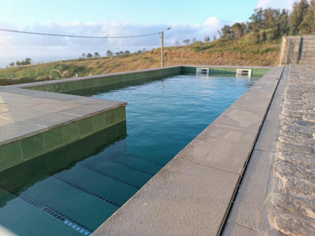 a swimming pool with blue water and a stone wall at Oak Tree House- Ponta do Pargo in Lombada Velha