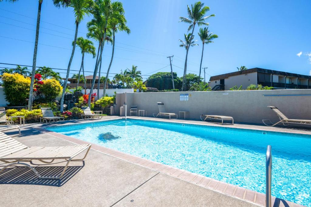a swimming pool with lounge chairs and palm trees at Walk to Napili Bay Beach! Mtn-View Lahaina Condo in Kahana