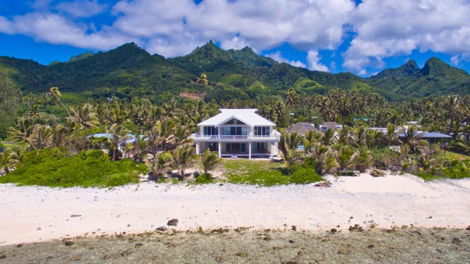 a house on the beach with mountains in the background at Seaside Beachfront Villas Rarotonga in Rarotonga