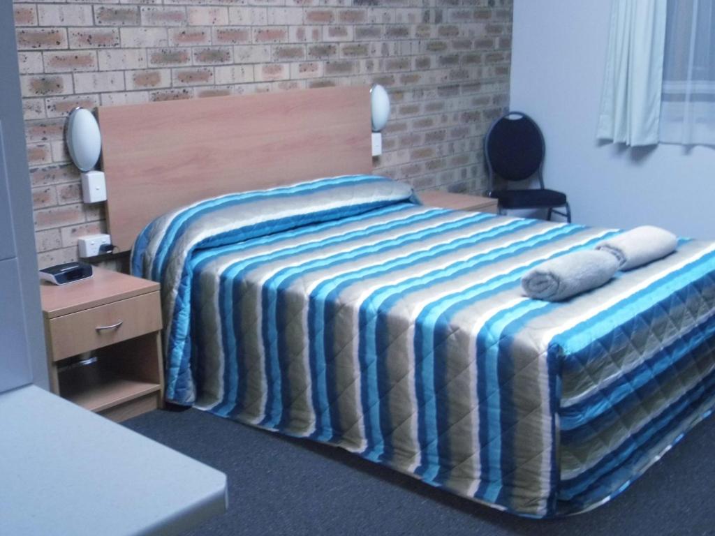 a bed with a striped blanket in a room at Nanango Fitzroy Motel in Nanango