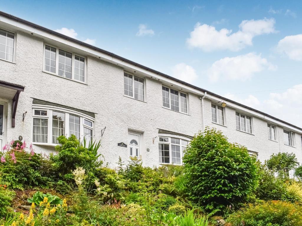 a white brick building with white windows and bushes at Oaklea Cottage in Windermere
