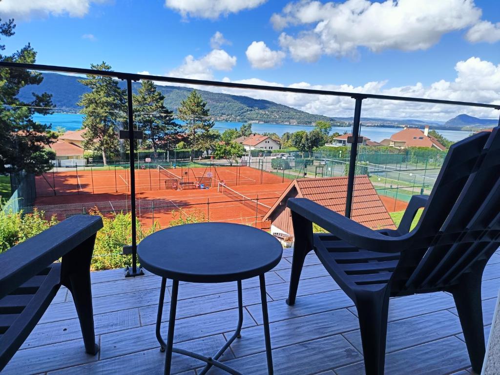 a balcony with two chairs and a table and a tennis court at Charmante Vue sur Lac in Veyrier-du-Lac