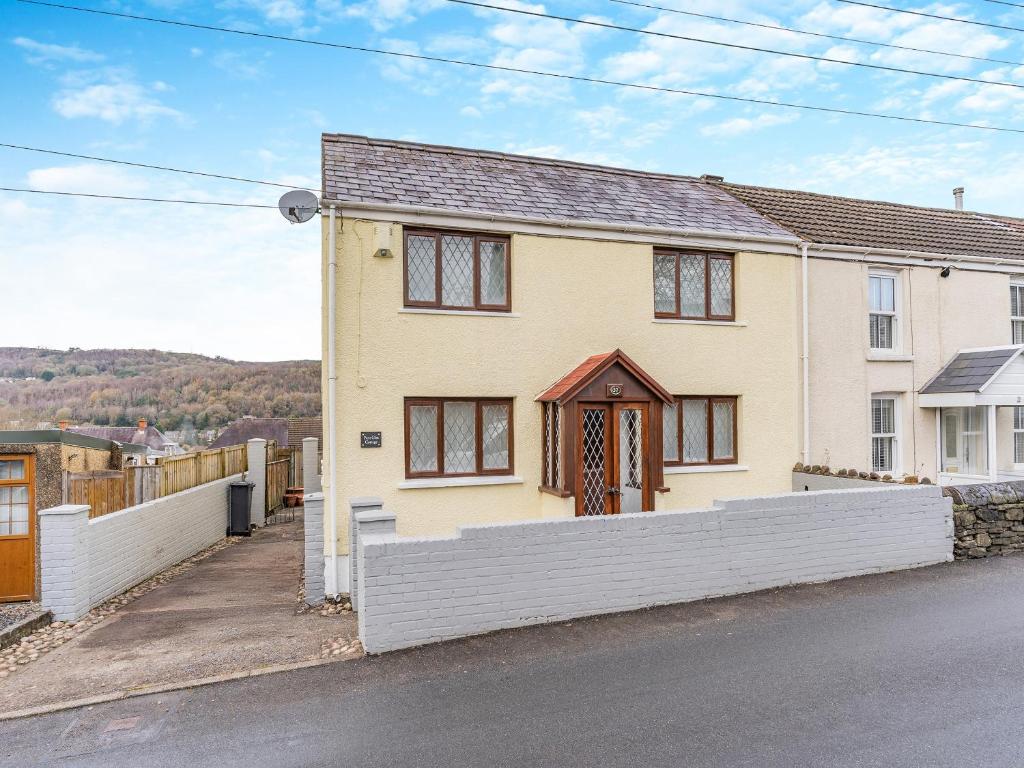 a yellow house with a white fence in front of it at Pant Glas Cottage in Pontardawe