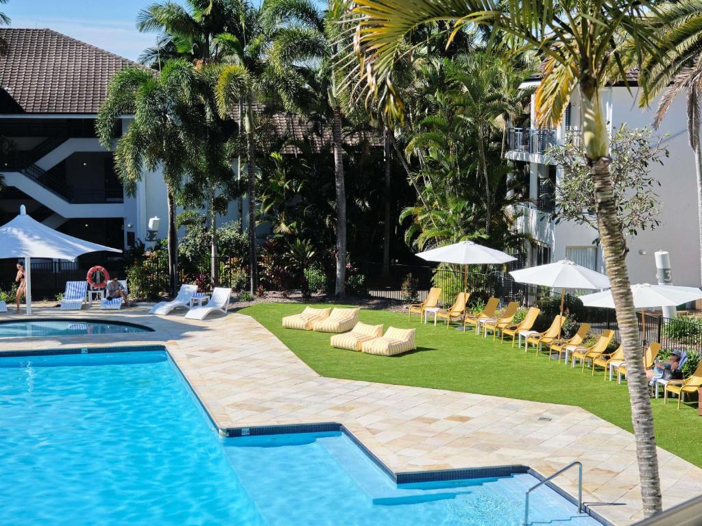 a pool with chairs and umbrellas next to a resort at Mercure Gold Coast Resort in Gold Coast