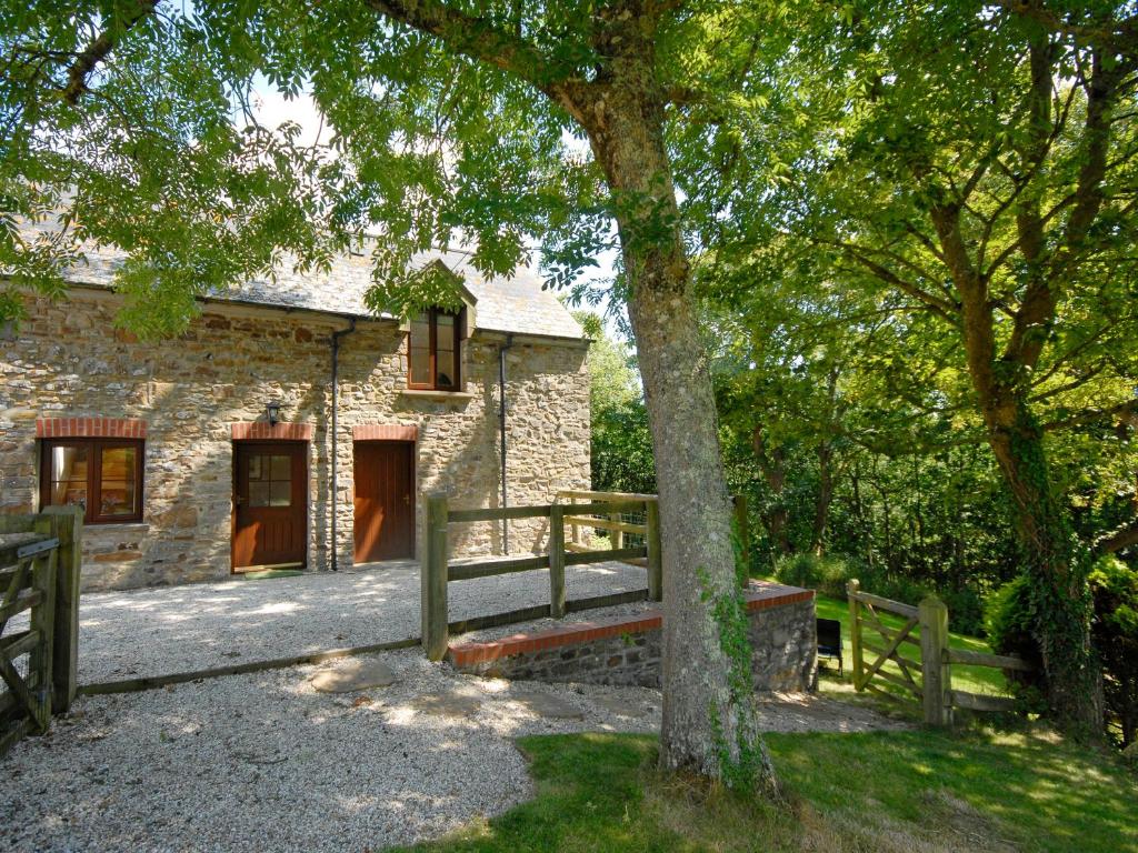 una casa de piedra con una valla de madera y un árbol en The Hayloft, en Walton West