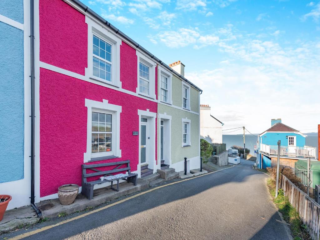 une maison rose avec un banc dans une rue dans l'établissement Bettys Cottage, à New Quay