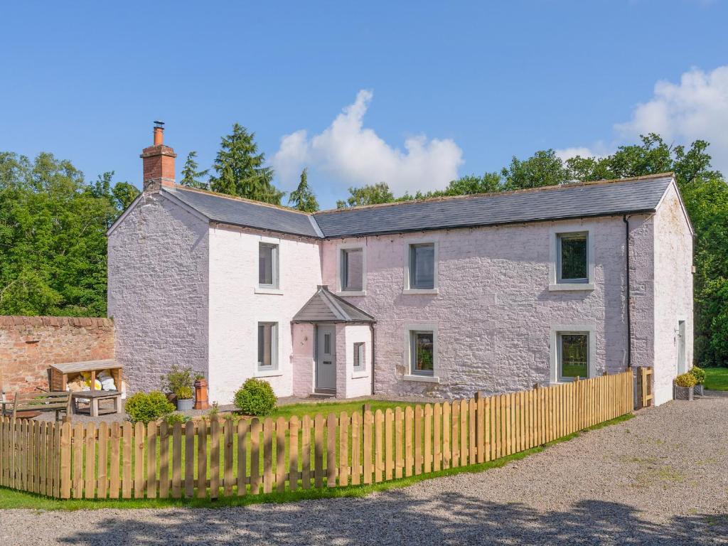 a large stone house with a wooden fence at Cleugh Foot in Longtown