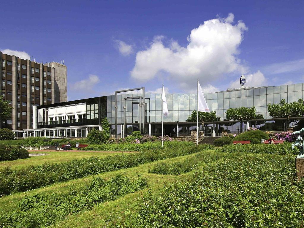 a large glass building with two white flags in front of it at Mercure Hotel Dortmund Messe in Dortmund
